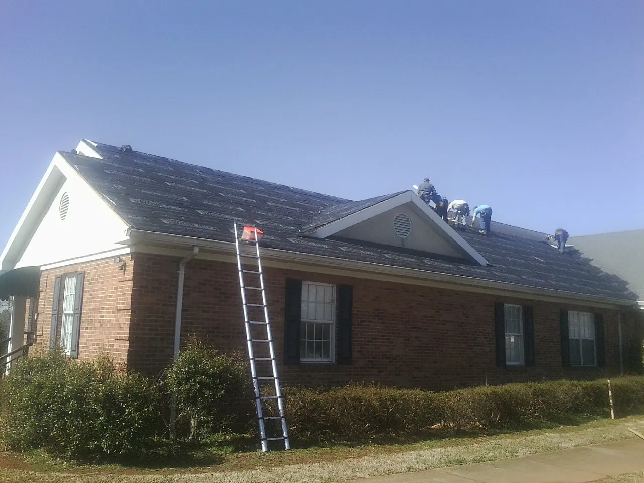 Crew tearing shingles off a brick ranch roof with a ladder set — Emergency Roof Repair work by our crew in Monetta