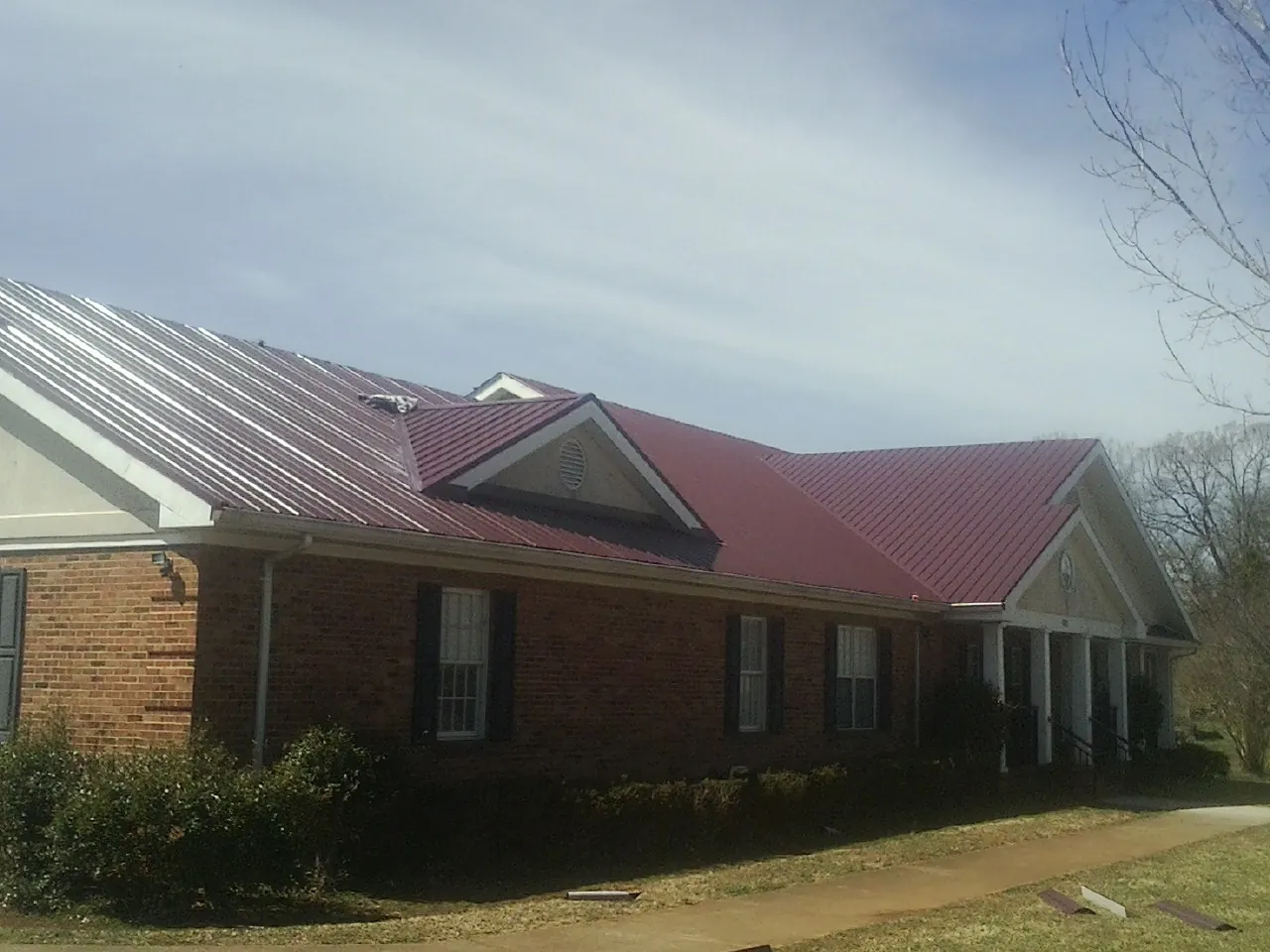 Red metal roof with gabled entries on a long brick building, from a Hail Damage Roof Repair job in Monetta