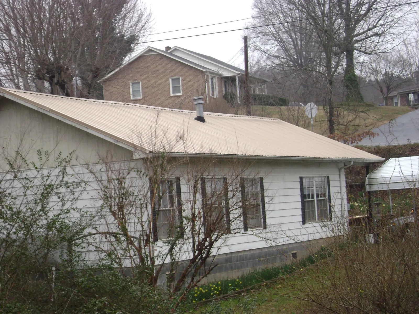 Tan metal roof on a white sided house set into a hillside — Commercial Roofing by Roofing Brothers in Monetta